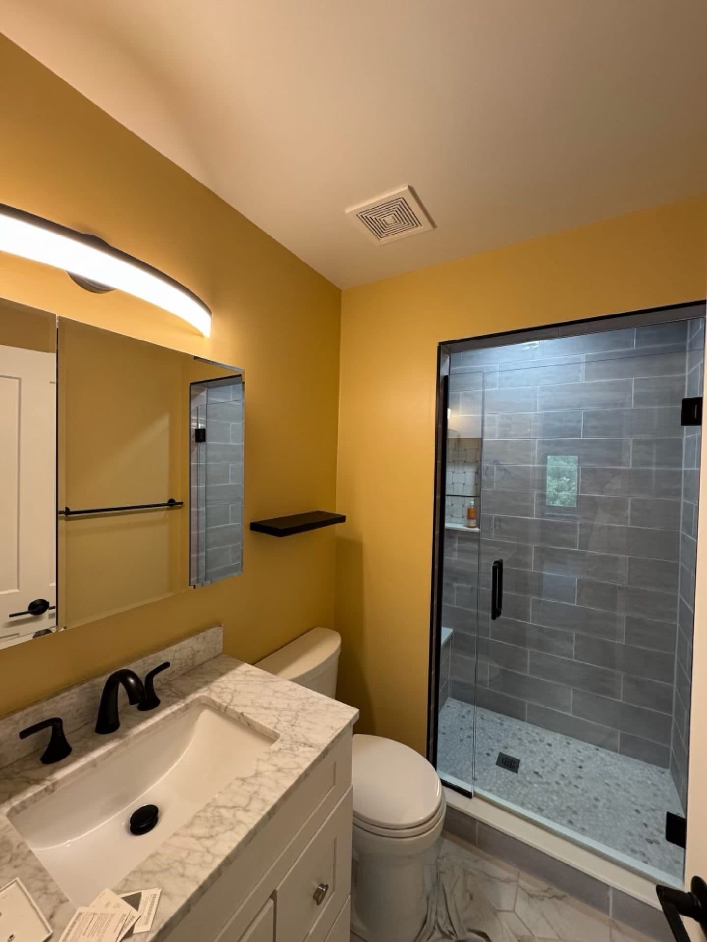 A bathroom painted a warm golden yellow with a white vanity and a tiled shower