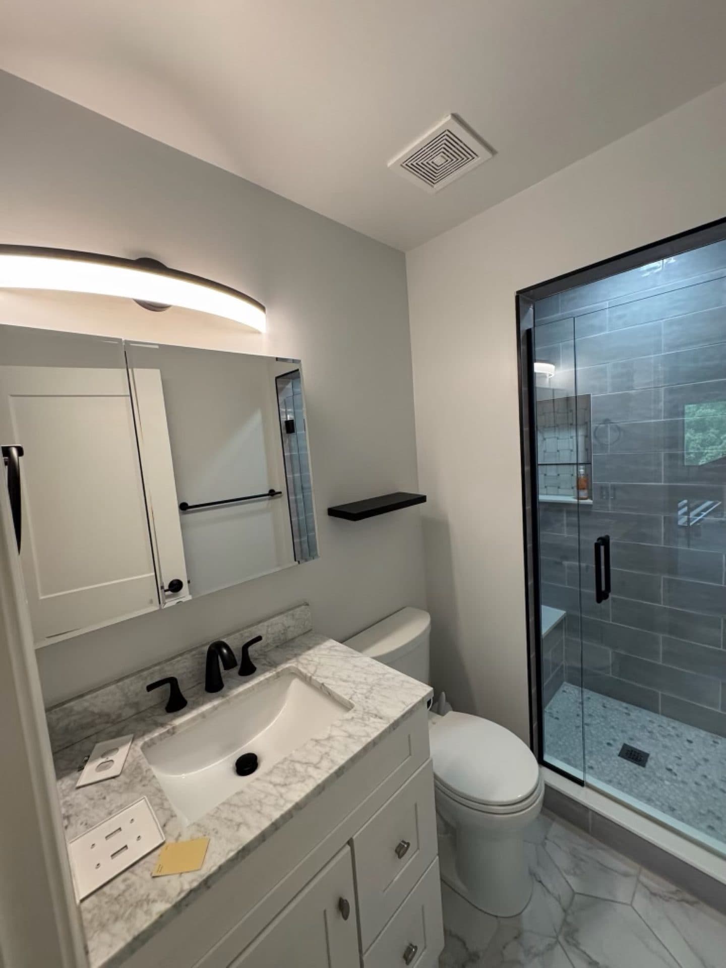 A bathroom with light gray walls, a white vanity, and a glass shower
