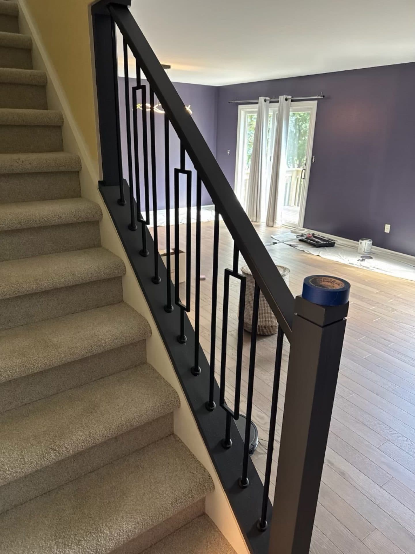 A staircase with a deep plum accent wall on the lower level and a black railing