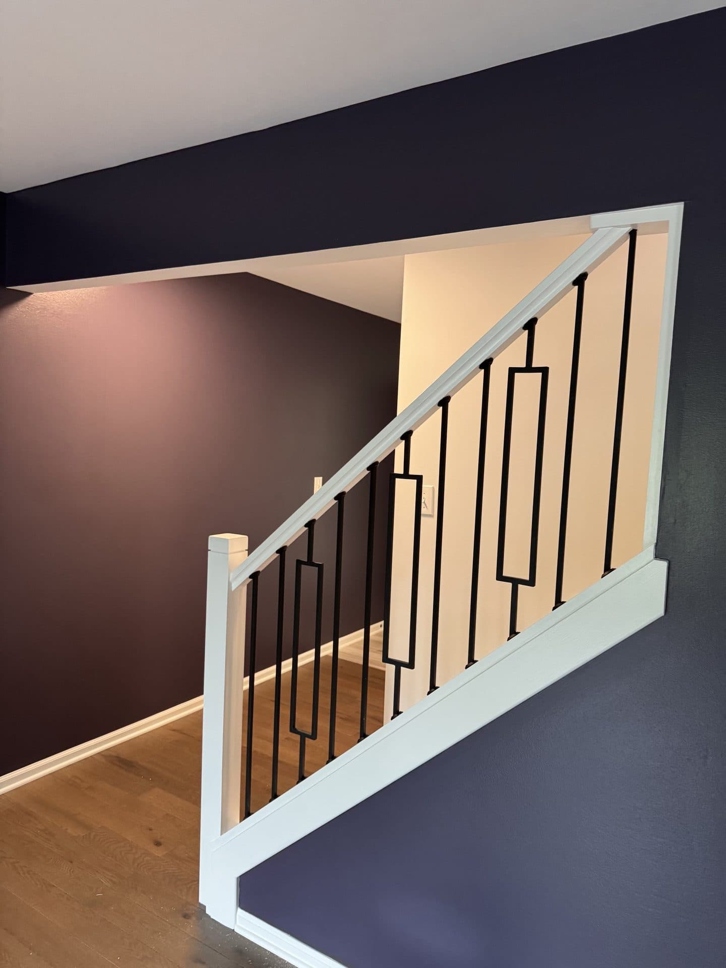 A stairwell with a deep navy accent wall, a white railing, and a wood floor